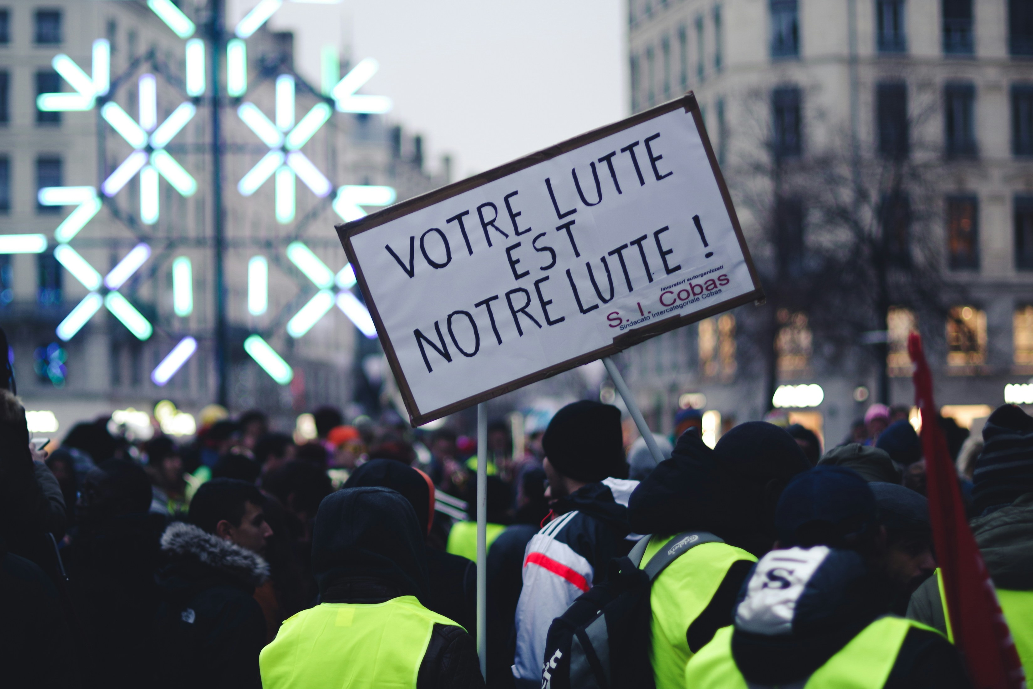A photo of a protest sign that reads: 'Votre Lutte Est Notre Lutte!' (Your fight is Our fight!)